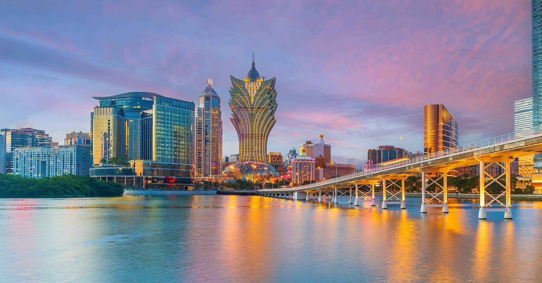 Macau skyline with casino resorts and city lights reflecting on water at sunset