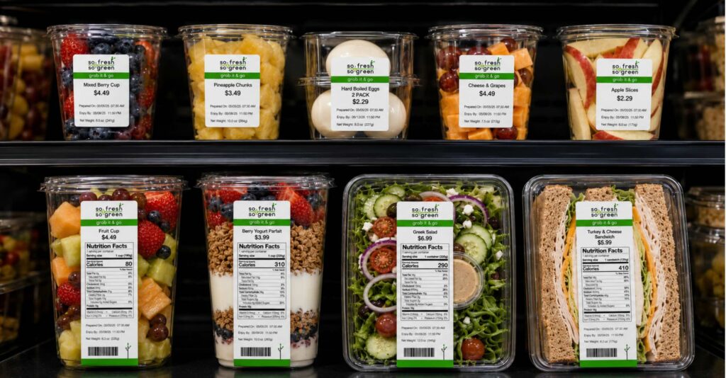 Fresh grab-and-go food items in a refrigerated display cooler with clear printed labels for prepared dates, use-by times, nutrition facts, and product information.